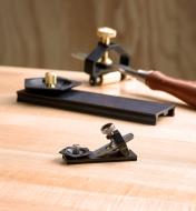 A small blade clamped in the miniature honing guide rests on the angle jig while a full-size version of the sharpening system appears in the background