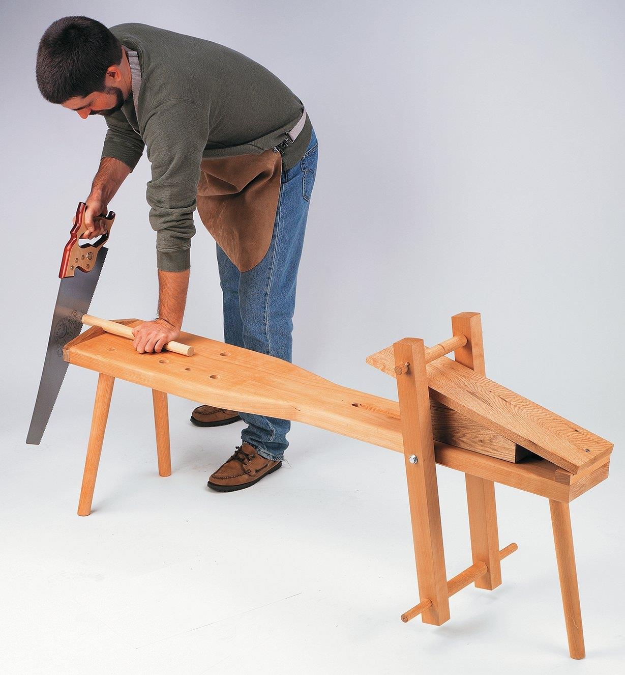 A man uses a shaving horse to saw a dowel