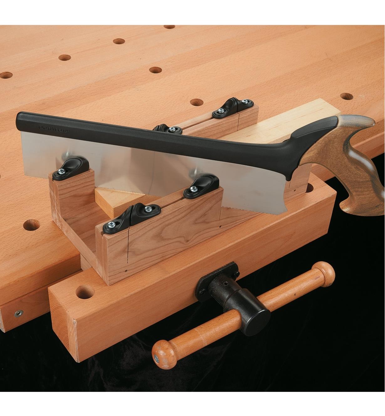 Using a completed miter box held in a workbench vise to cut wood at an angle