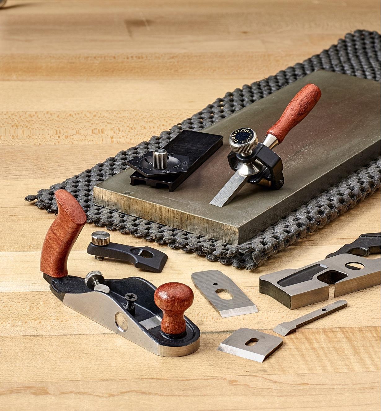 A chisel blade held in the miniature honing guide sits beside the angle jig on a sharpening stone with other small blades nearby