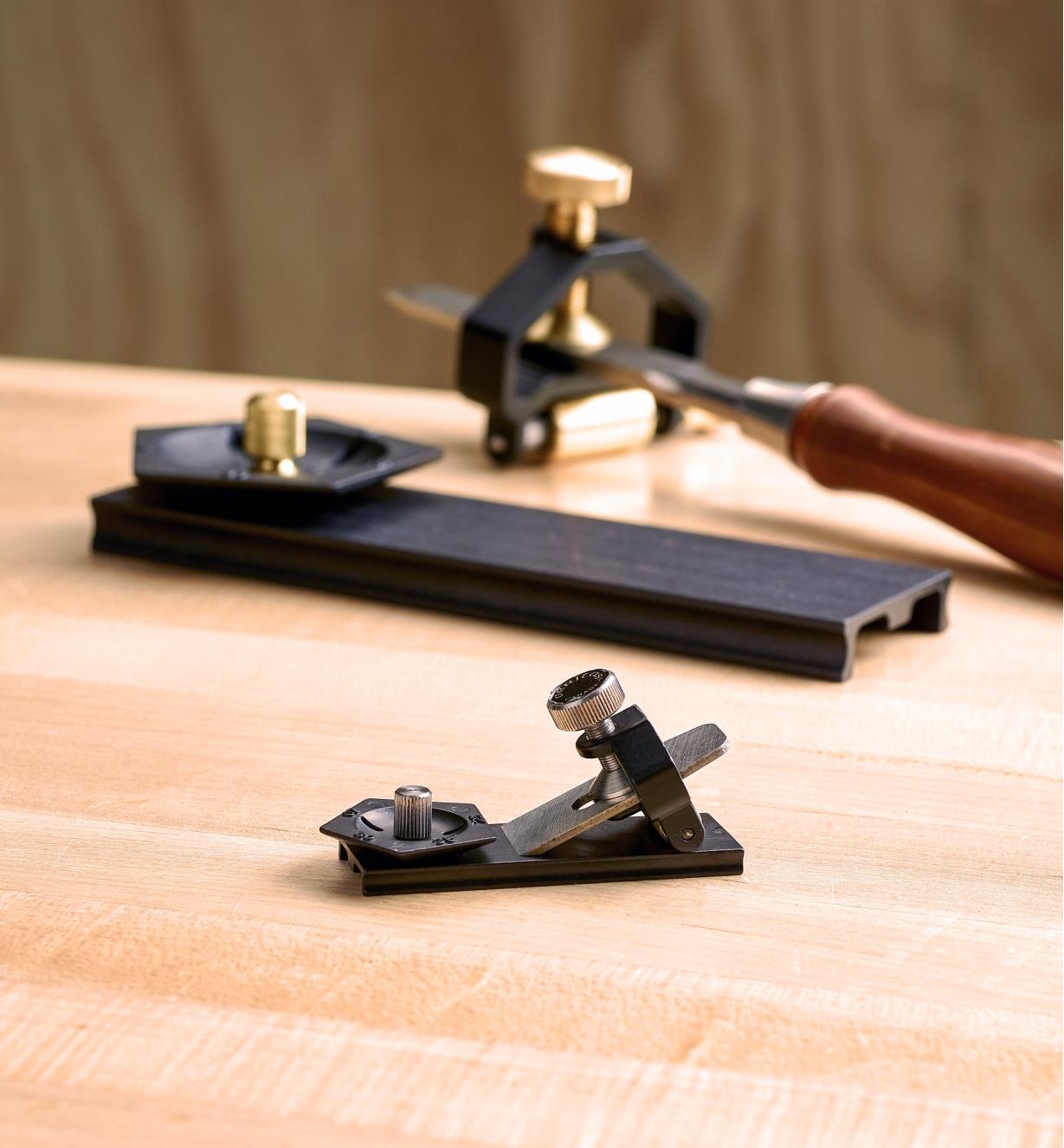 A small blade clamped in the miniature honing guide rests on the angle jig while a full-size version of the sharpening system appears in the background