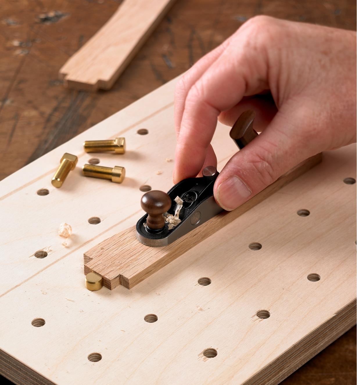 A Veritas miniature surface dog restrains a workpiece as it is being planed with a Veritas miniature bench plane
