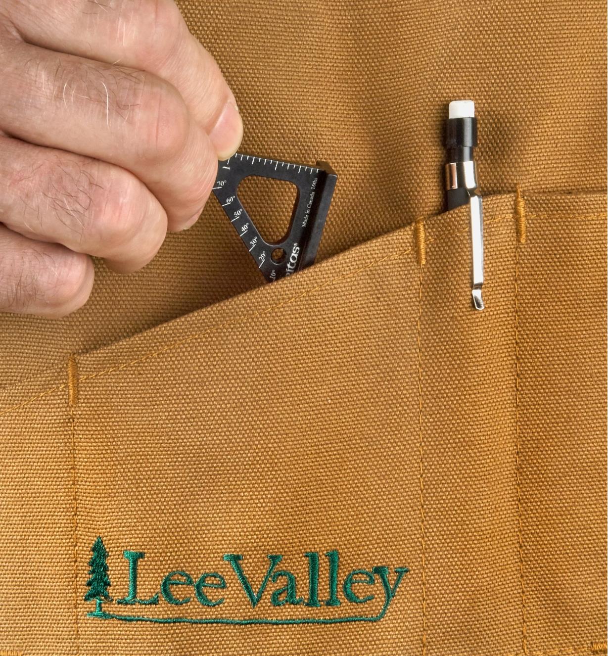 A woodworker slips a Veritas 1 1/2"" Pocket Layout Square into the pocket of a workshop apron