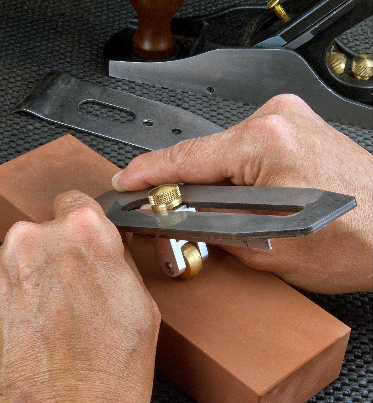 A woodworker uses a Lee Valley replica honing guide to sharpen a plane blade on a sharpening stone